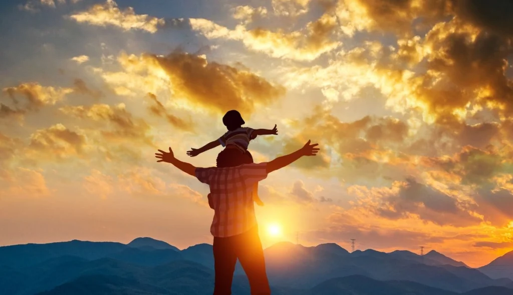 A father carrying his child on his back standing at the top of a mountain