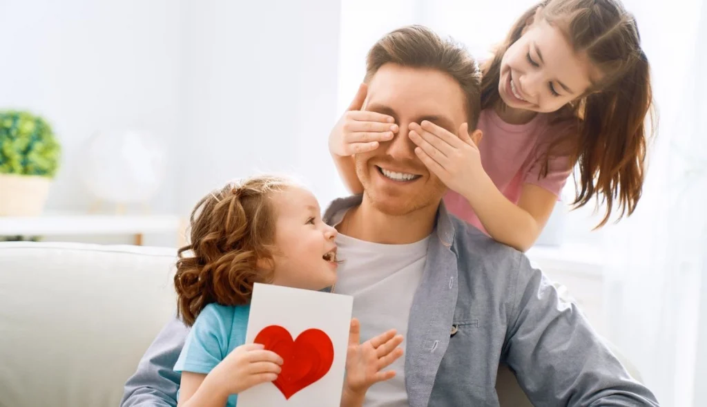 two daughters are playing with their dad holding a fathers day card